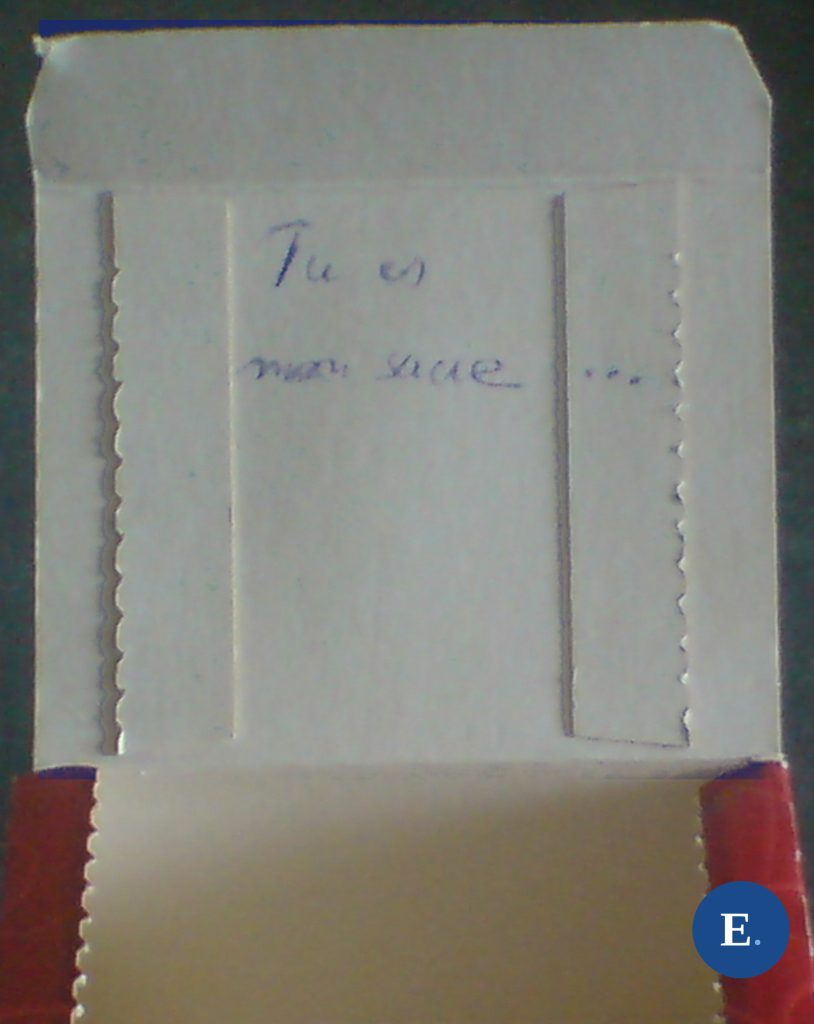 Couvercle relevé d’une boîte de sucre en morceaux Saint Louis ; deux lignes manuscrites à l’encre bleue sur le carton intérieur du rabat ; médaillon E. bleu en bas à droite.