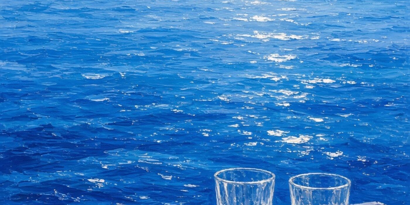 Une mer bleue scintillante, deux verres sur une nappe blanche.